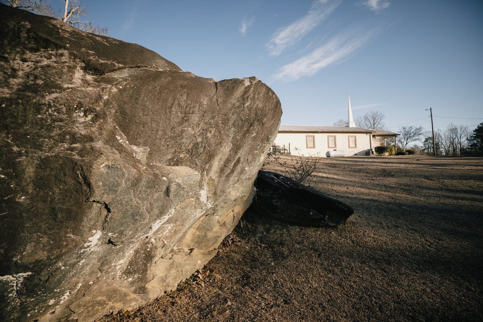 A large soapstone rock outcropping on the church grounds, with Soapstone Baptist Church and its steeple visible in the background