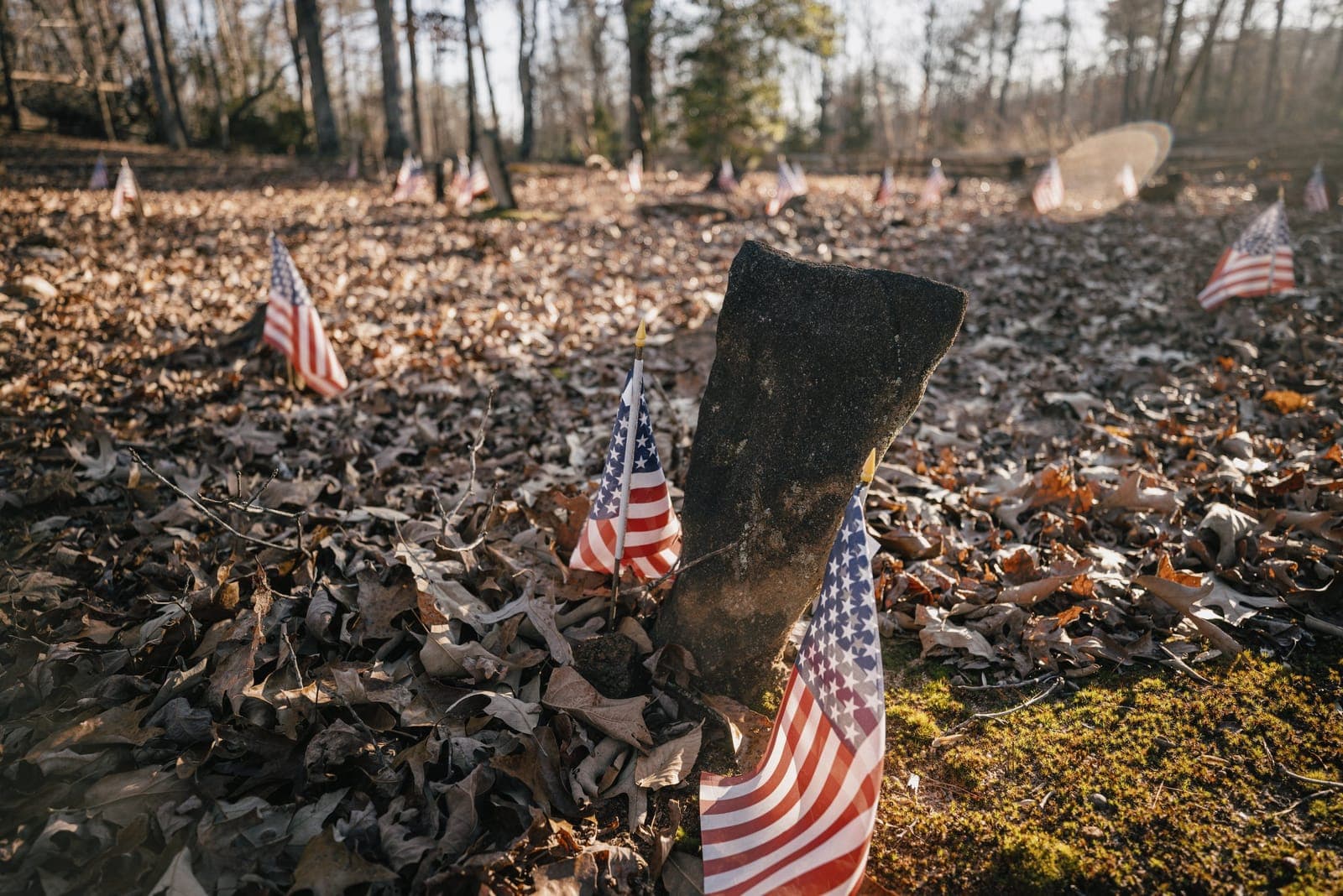 A weathered headstone marked with small American flags in the historic Soapstone cemetery